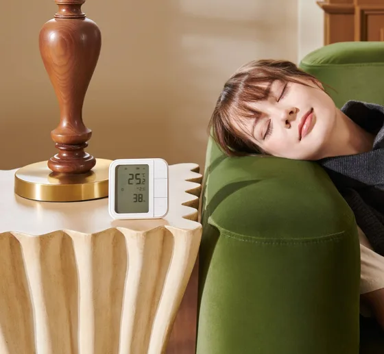 Persona durmiendo en un sillón junto a un control de clima Aqara W100 que marca 25 grados